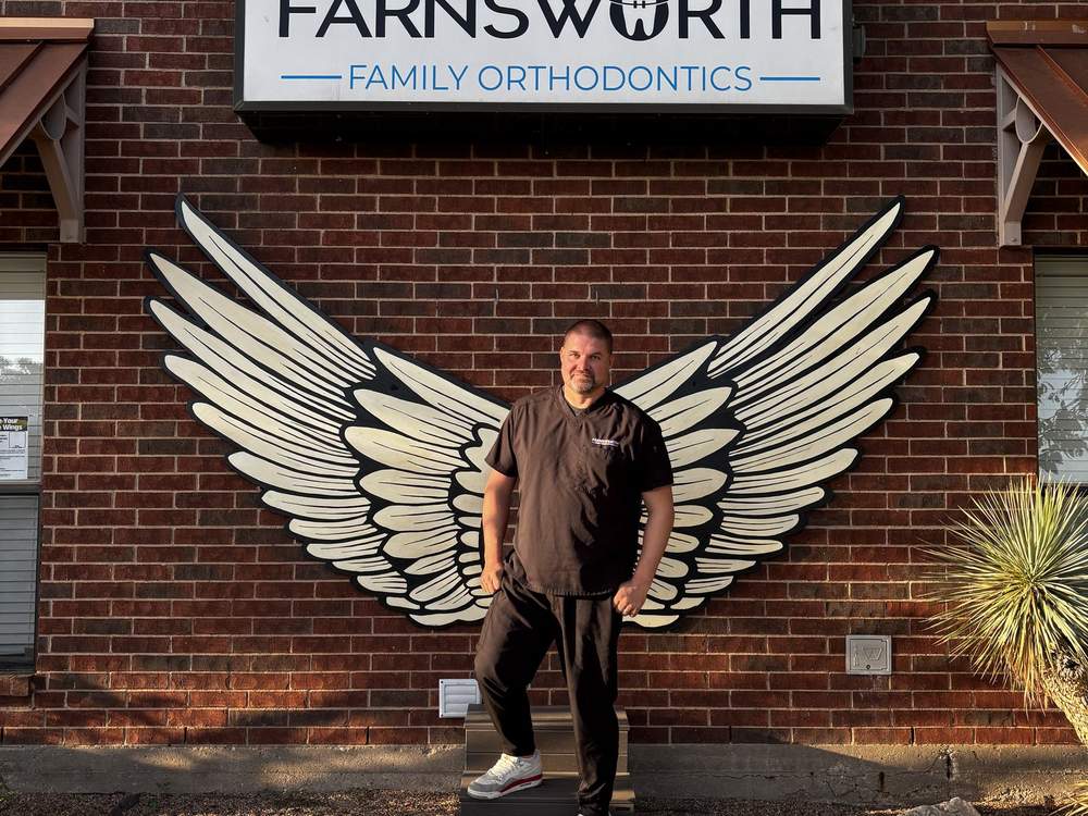 Dr. Brimhall in front of the angel wings mural beneath the Farnsworth Family Orthodontics sign at the San Angelo office